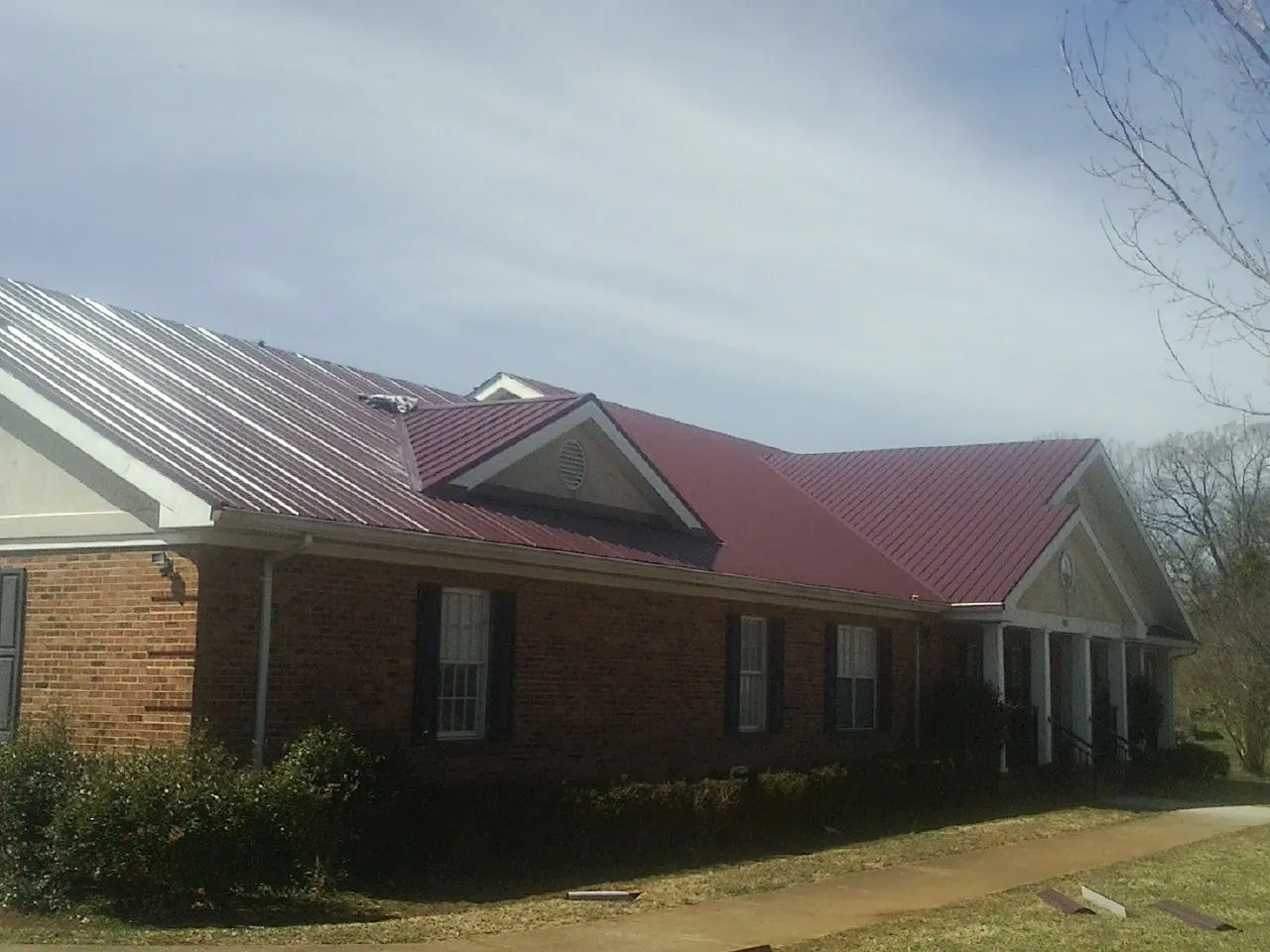 Red metal roof with gabled entries on a long brick building, from a Hail Damage Roof Repair job in Canby