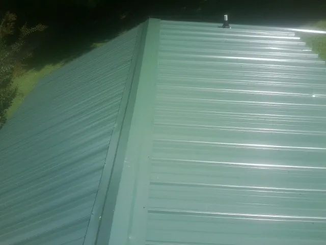 New green metal panels meeting at the ridge of a roof — Flat Roof Repair work by our crew in Canby