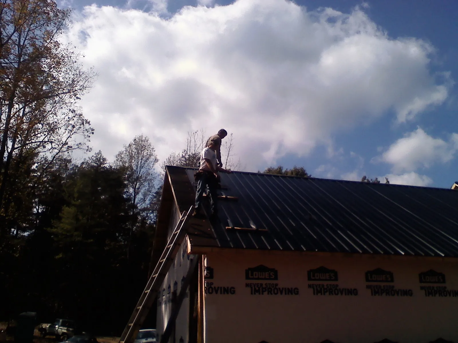 Roofer fastening dark metal panels high against a cloudy sky, from a Roof Inspection job in Canby